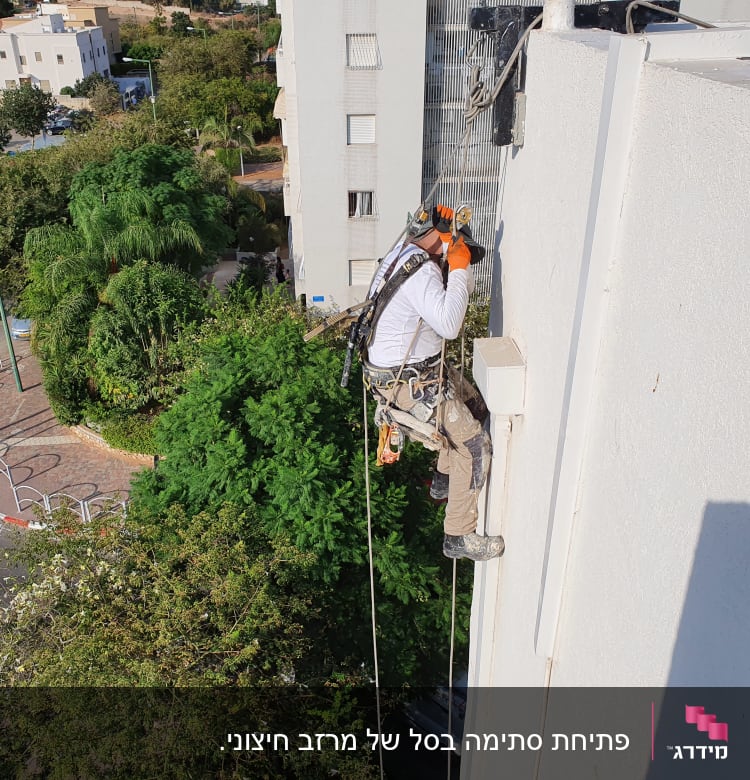 אדם בעבודת גובה על קיר בניין עם ציוד בטיחות